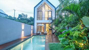 A modern house with a swimming pool, a covered outdoor seating area, and lush greenery.