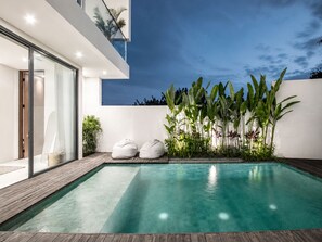 A modern outdoor pool area with a wooden deck, two bean bags, and tropical plants. - Casa Rio 3BR Enclosed Living & Pool (Keroboken Kelod)