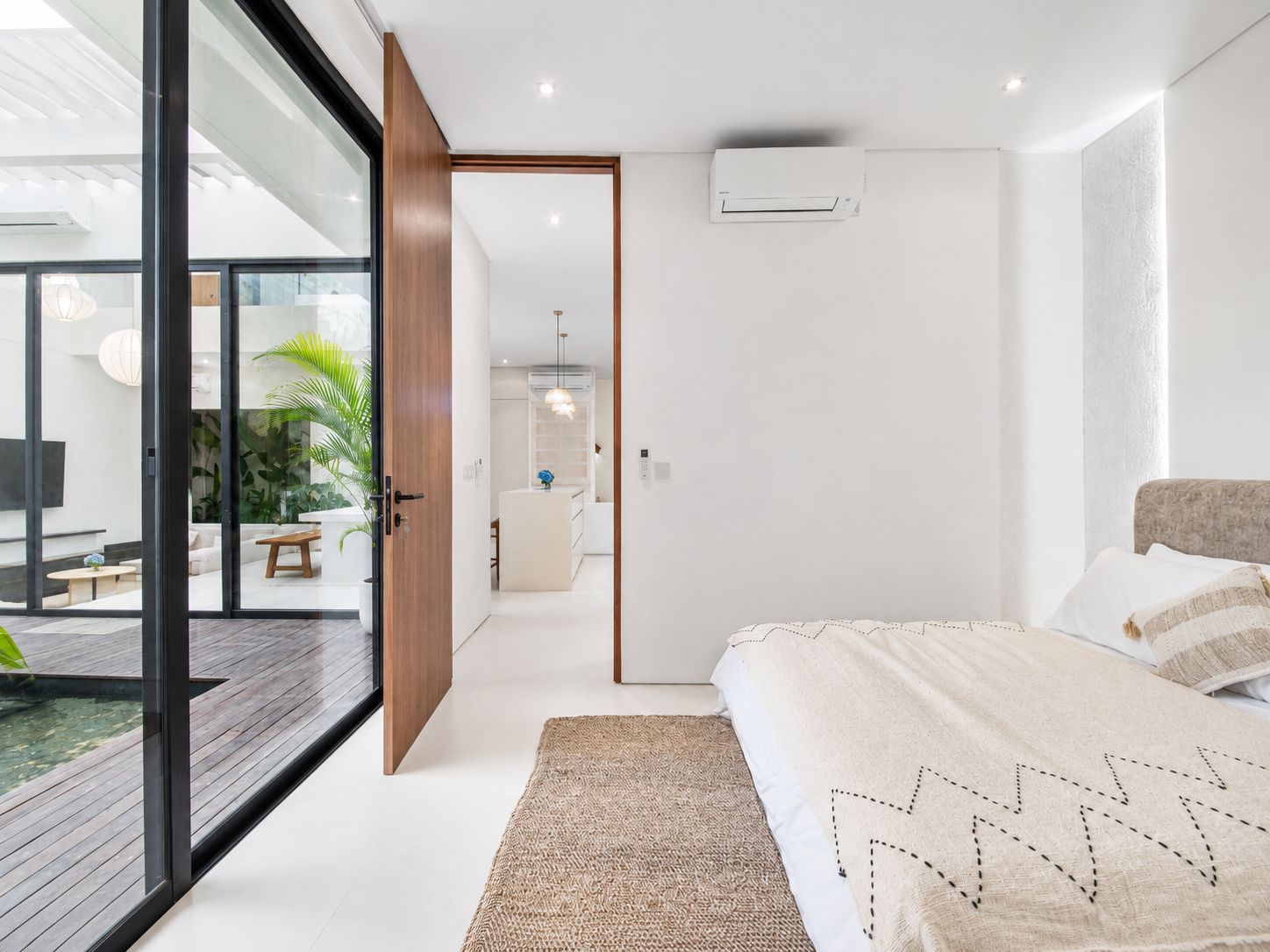 Un dormitorio moderno con una cama grande, un vidrio que da a un espacio exterior y una pequeña cocina.