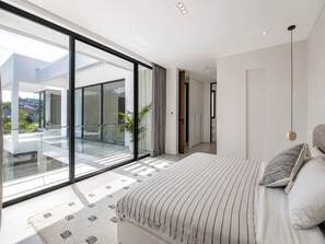A modern bedroom with a large bed, a view of the outdoors, and a sliding glass door leading to a balcony. - Casa Rio 3BR Enclosed Living & Pool (Keroboken Kelod)