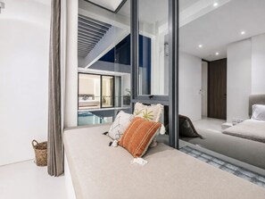 A modern bedroom with a large bed, a glass wall, and a view of a pool. - Casa Rio 3BR Enclosed Living & Pool (Keroboken Kelod)
