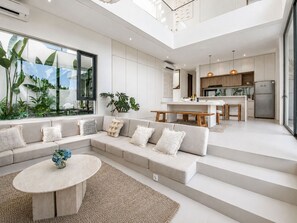 A modern living space with a sectional sofa, a round coffee table, and a kitchen area with a refrigerator and dining set. - Casa Rio 3BR Enclosed Living & Pool (Keroboken Kelod)