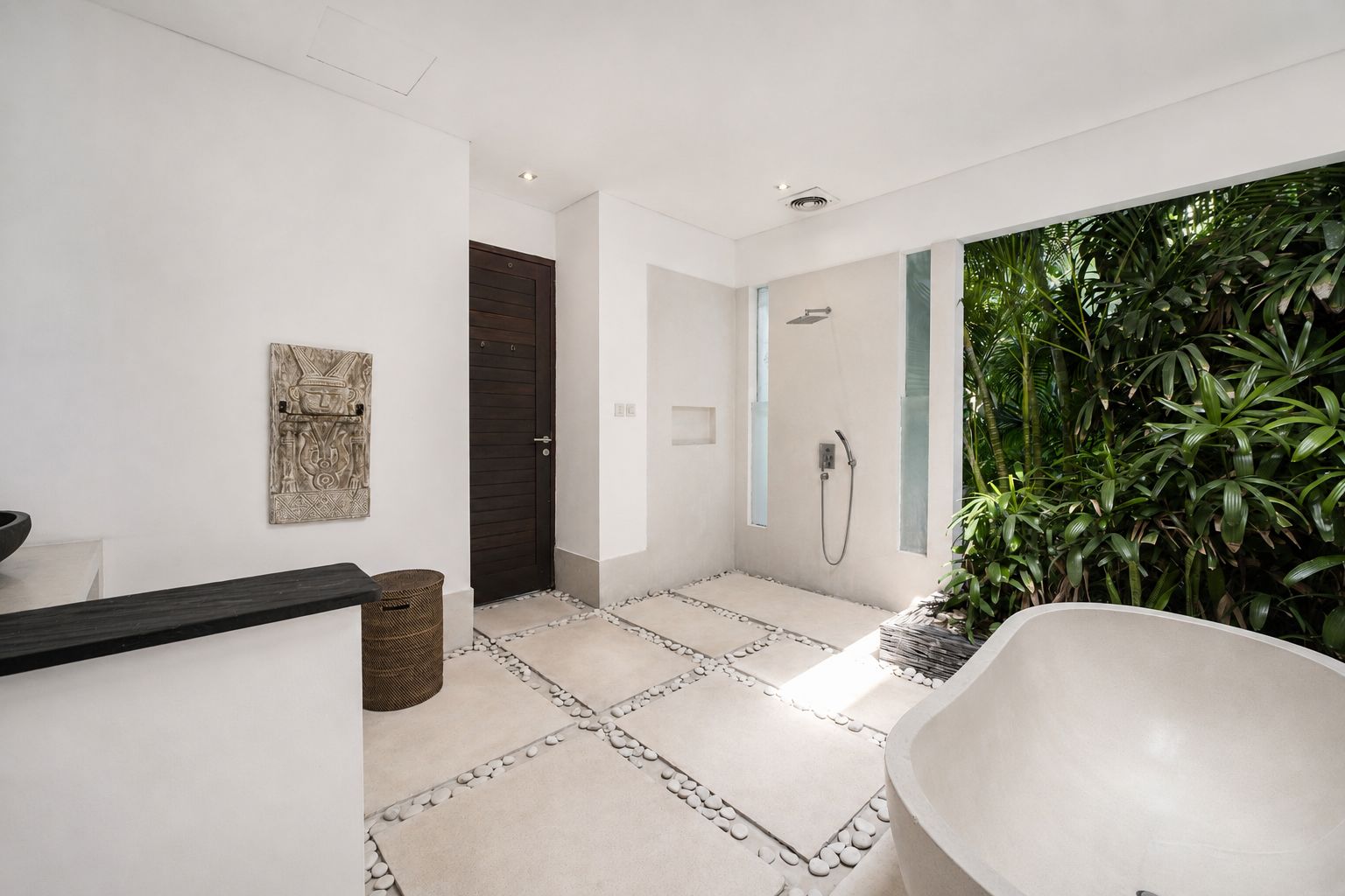 A modern bathroom with a bathtub, shower, and a large window with greenery outside.