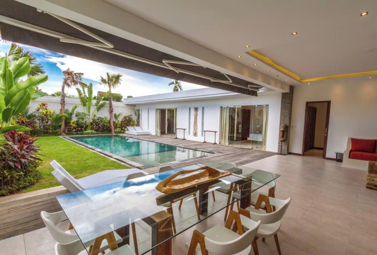 Un interior moderno con una mesa de comedor de vidrio, sillas blancas, una piscina y un jardín bien cuidado.