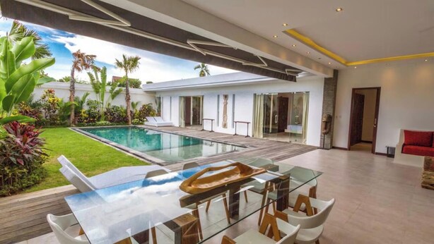 Ein modernes Interieur mit einem Glastisch, weißen Stühlen, einem Pool und einem gepflegten Garten.