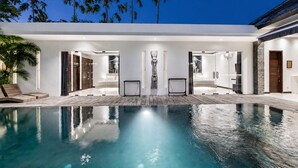Ein moderner Poolbereich mit klarem Pool, Liegestühlen und einem von Glas umschlossenen Spa-Bereich.