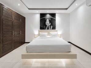 A modern bedroom with a large bed, wooden wardrobe, and a wall-mounted artwork. - Villa Juna Serene 3BR Hideaway Seminyak (Seminyak)
