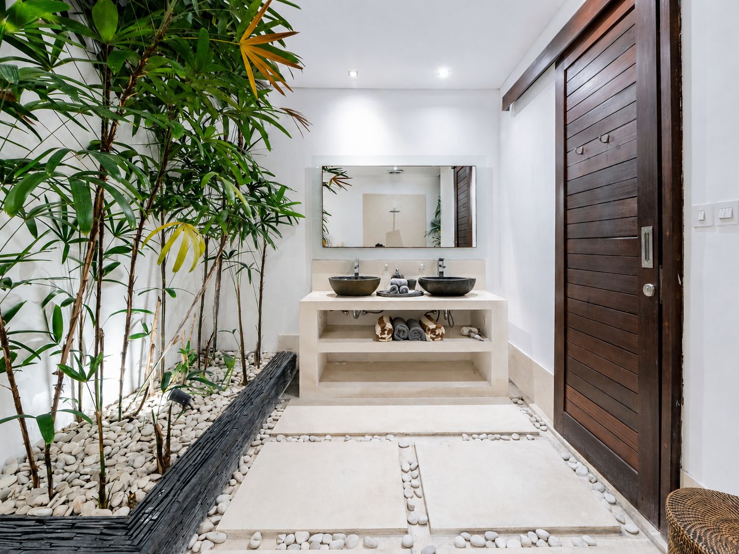 A bathroom with a modern design, featuring a large mirror, two sinks, and a wooden door.