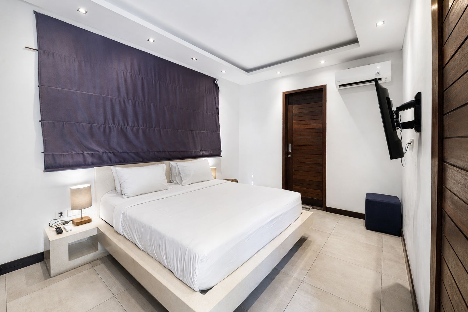 A modern bedroom with a large bed, bedside tables, a TV, and a wooden door.