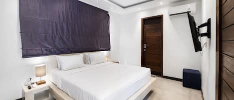 A modern bedroom with a large bed, bedside tables, a TV, and a wooden door.