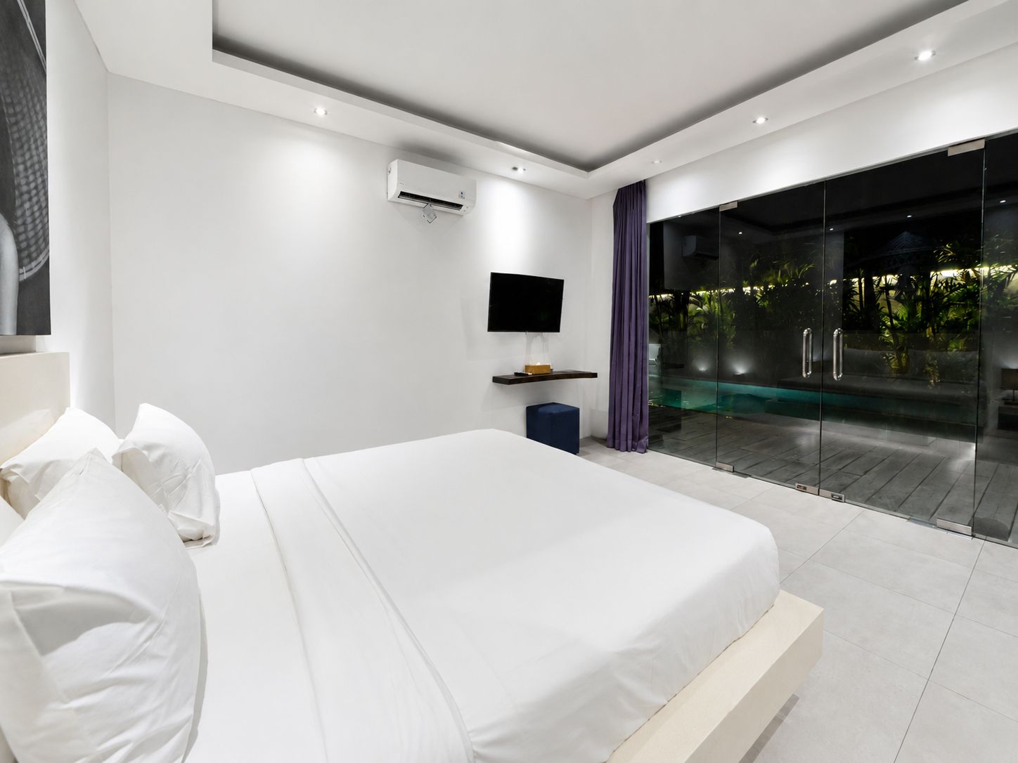 A modern bedroom with a large bed, a flat-screen TV, an air conditioning unit, and a glass door leading to an outdoor area.