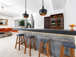 A modern kitchen with a bar area, stone countertops, and wooden stools. - Villa Juna Serene 3BR Hideaway Seminyak (Seminyak)