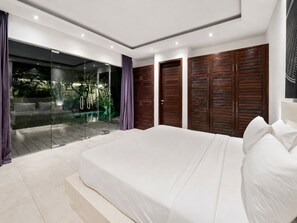 A bedroom with a large bed, wooden wardrobes, and a glass door leading to a pool area. - Villa Juna Serene 3BR Hideaway Seminyak (Seminyak)