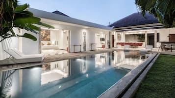 A modern house with a swimming pool, a covered patio, and a well-maintained lawn.