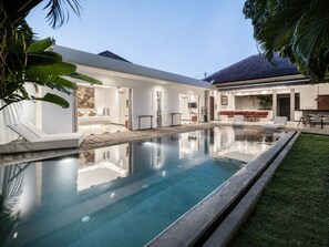 Una casa moderna con piscina, un patio cubierto y un césped cuidado.