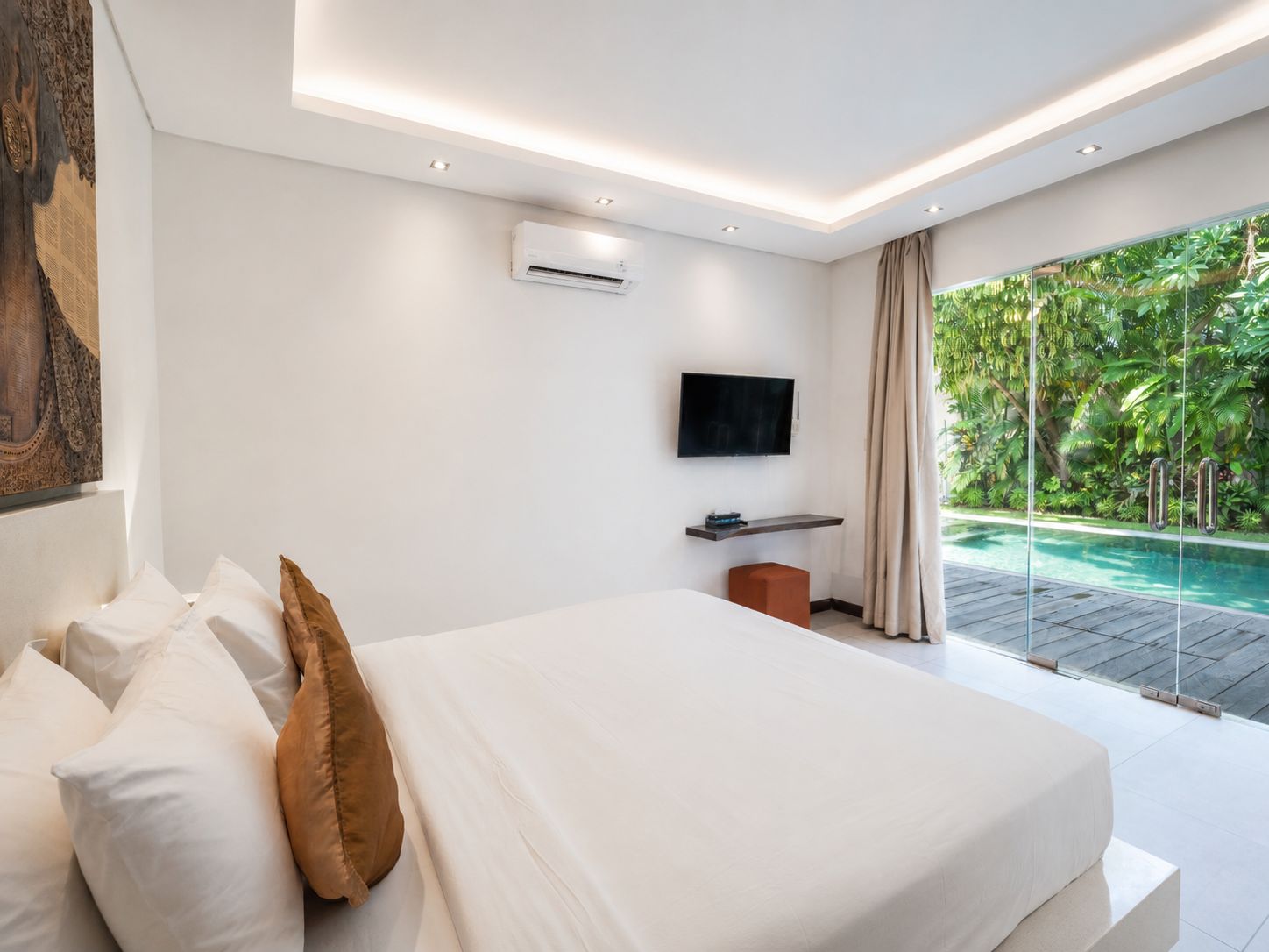 A modern bedroom with a large bed, a flat-screen TV, an air conditioning unit, and a view of a swimming pool.