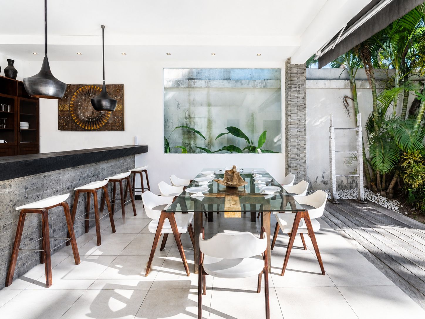 A modern dining area with a glass table, white chairs, and a stone wall.