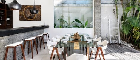 A modern dining area with a glass table, white chairs, and a stone wall.
