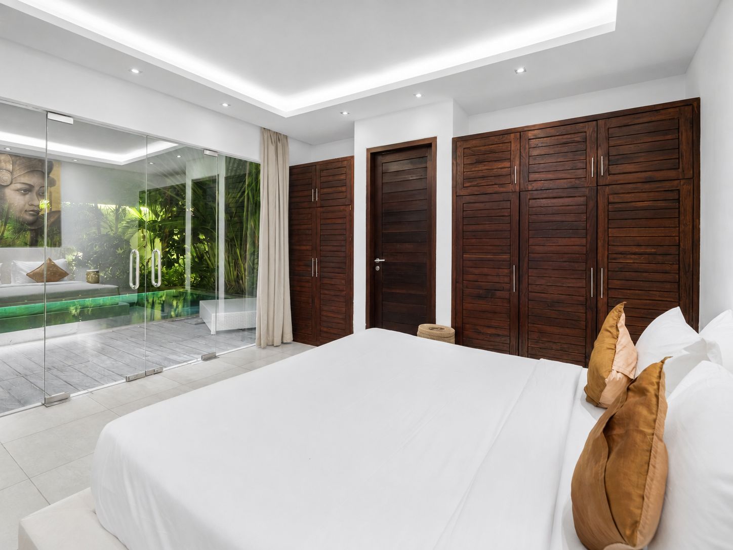 A modern bedroom with a large bed, wooden wardrobes, a glass door leading to a balcony, and a view of greenery.