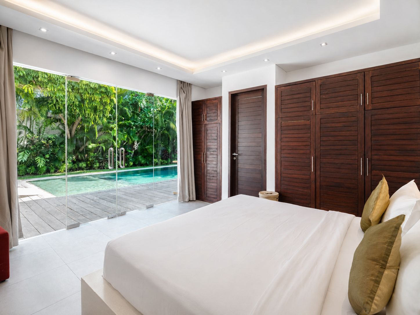 A bedroom with a large bed, a view of a swimming pool, and wooden wardrobes.
