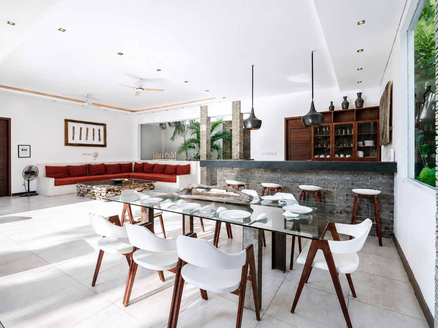 A modern dining area with a glass table, white chairs, and a red sofa in the background.