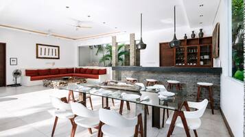 A modern dining area with a glass table, white chairs, and a red sofa in the background.