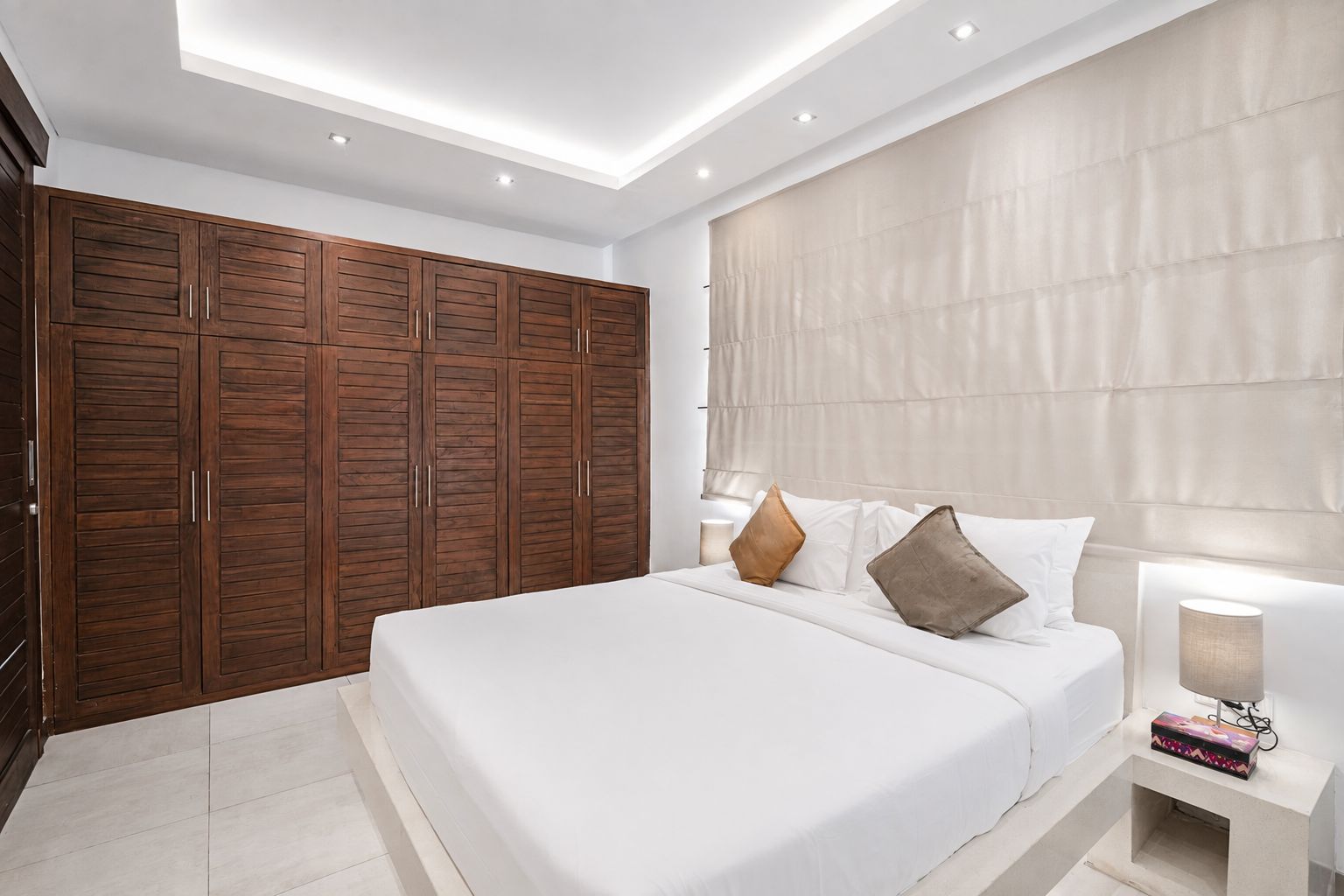 A modern bedroom with a large bed, a wardrobe, and a bedside table with a lamp.
