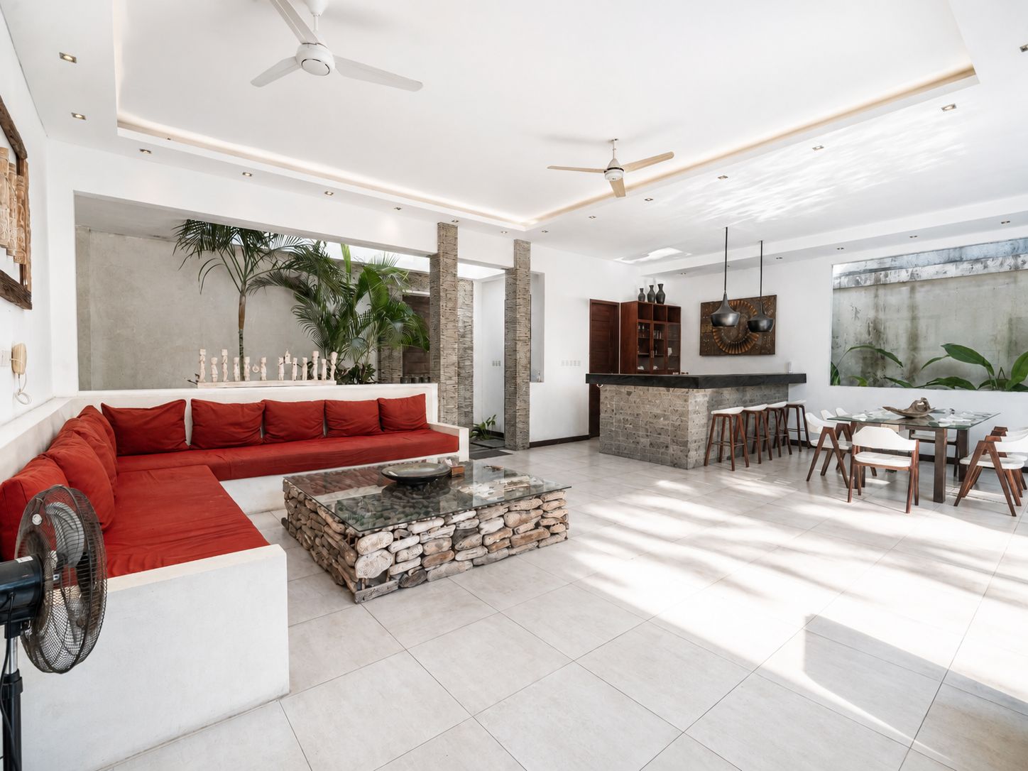 A modern living room with a red sofa, a stone coffee table, and a dining area with a bar.