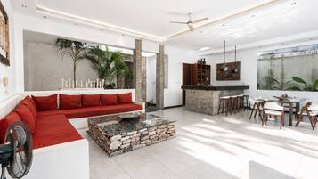 A modern living room with a red sofa, a stone coffee table, and a dining area with a bar.
