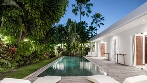 A poolside area with lounge chairs, a wooden deck, and lush tropical vegetation. - Villa Saha Elegant 3BR Pool Oasis Seminyak (Seminyak)