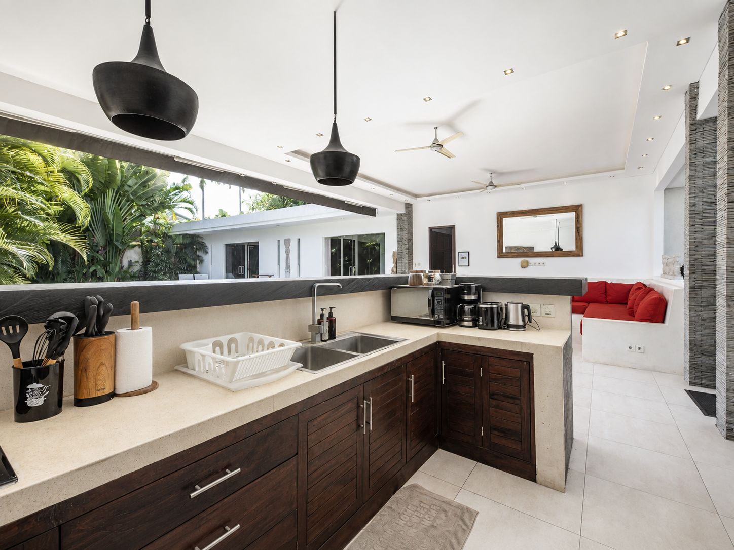 Cocina moderna con armarios de madera oscura, una isla grande y vistas a una casa y follaje exterior.