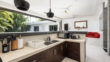 Une cuisine moderne avec des meubles en bois foncé, un grand îlot central et une vue sur une maison et la verdure environnante.