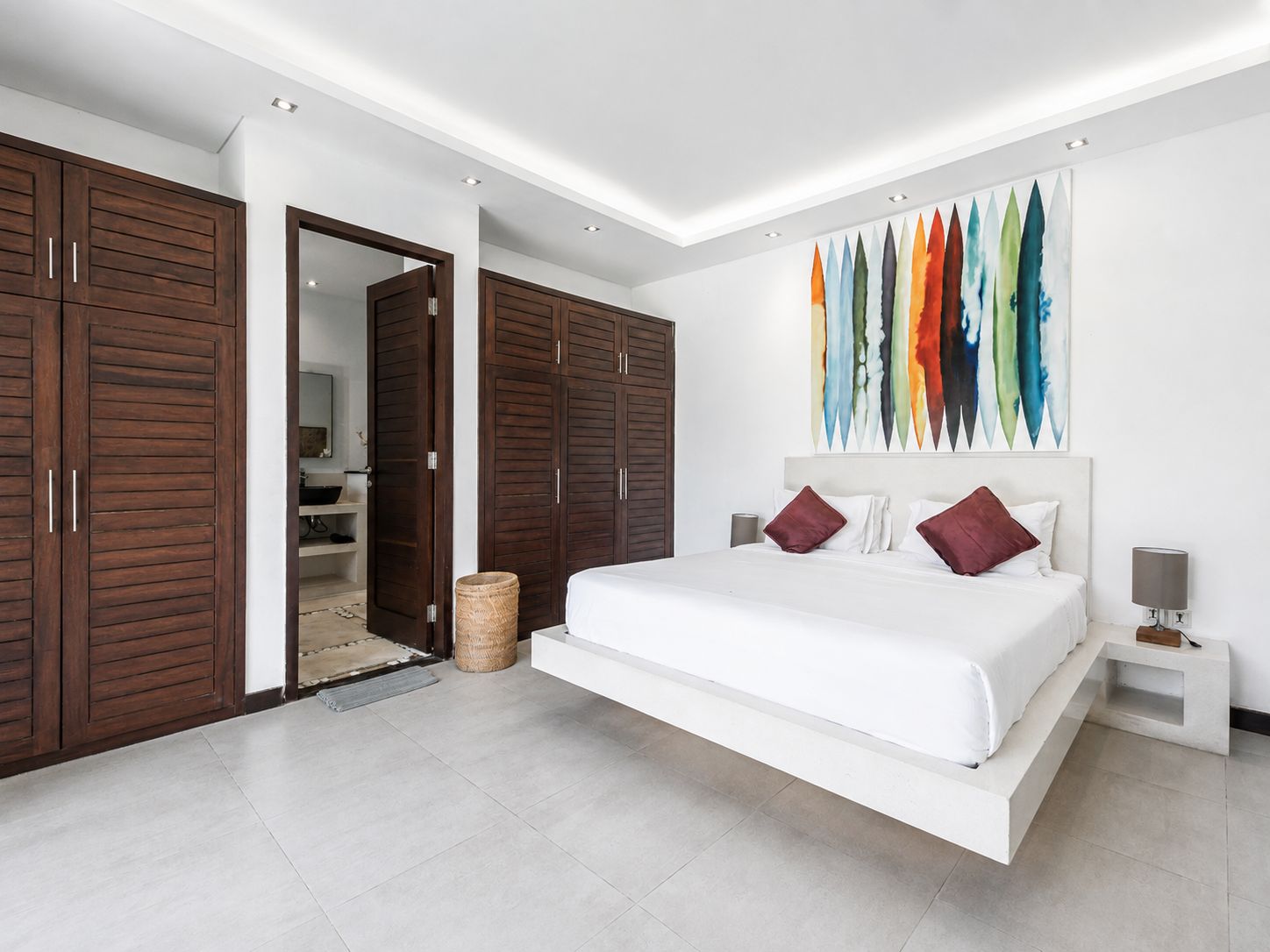 Un dormitorio moderno con una cama grande, armarios de madera y un cuadro abstracto colorido.