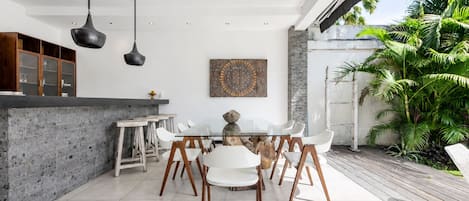 A modern kitchen with a dining area, featuring a stone countertop, white chairs, and pendant lighting.