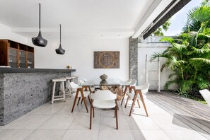 Una cocina moderna con comedor, que cuenta con encimera de piedra, sillas blancas e iluminación colgante.
