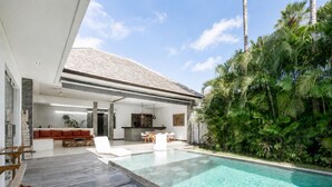 Ein modernes Haus mit Schwimmbad, einer Holzterrasse und üppiger Bepflanzung.