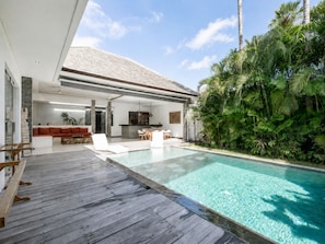 Een modern huis met zwembad, een houten terras en weelderige begroeiing.