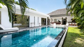 A modern pool area with a clear blue pool, surrounded by a white building with glass doors and a patio area with lounge chairs.