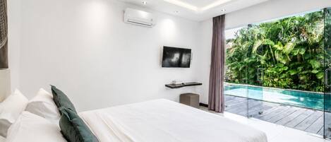 A modern bedroom with a large bed, a flat-screen TV, and a view of a swimming pool.