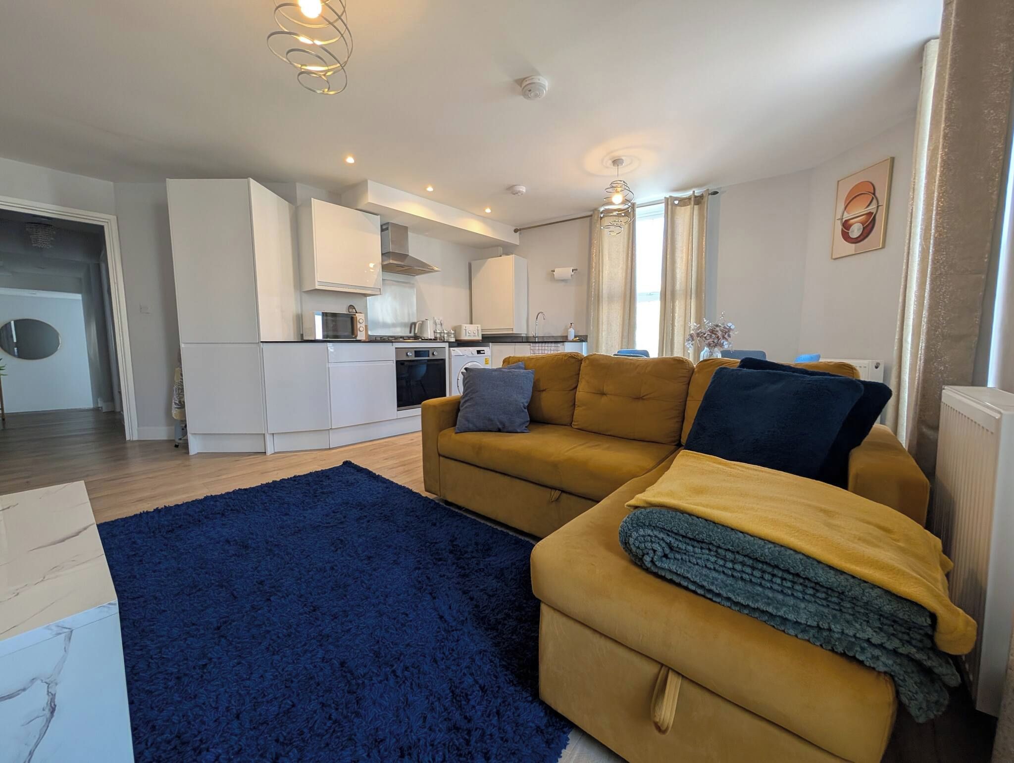 A compact living space with a sofa, a blue rug, and a kitchenette in the background.