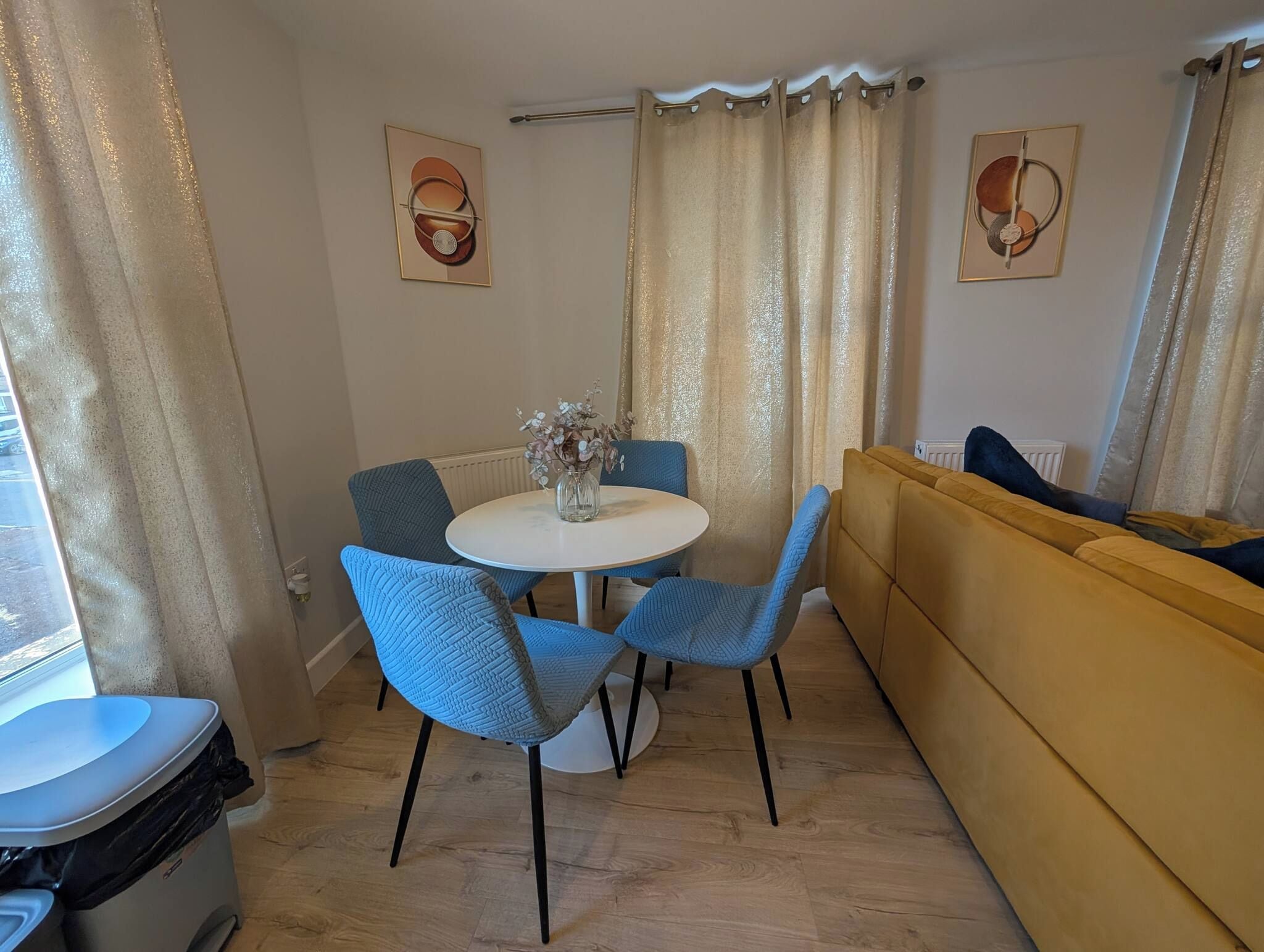 A dining area with a round table, blue chairs, and a yellow sofa.