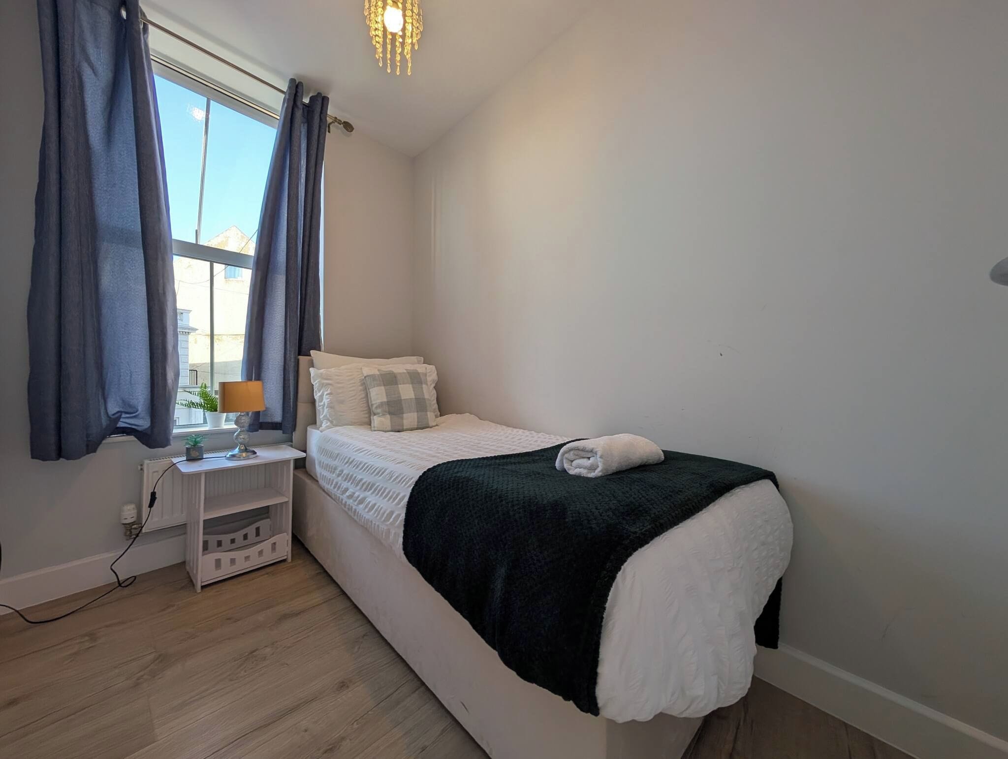 A bedroom with a bed, a nightstand, a lamp, and a window with curtains.
