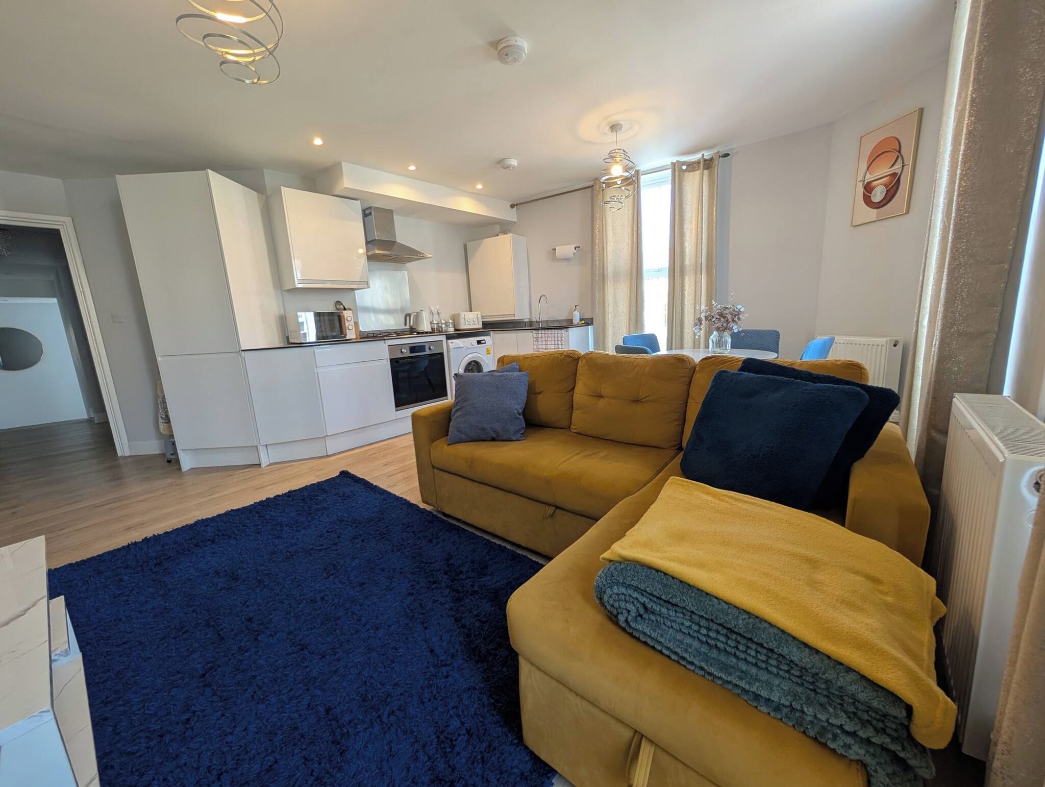 A modern living room with a sofa, a blue rug, and a kitchen in the background.
