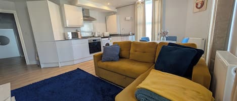 A modern living room with a sofa, a blue rug, and a kitchen in the background.