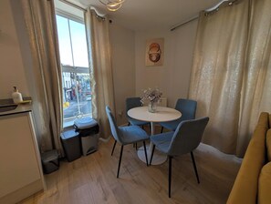 En kompakt opholdsstue med spiseplads, et lille tekøkken og udsigt til gaden.