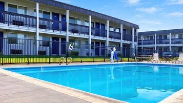 A multi-story hotel with a swimming pool, balconies, and a fenced area.