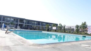 A swimming pool with a metal ladder, surrounded by a fence, and a multi-story building in the background.