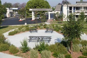 An outdoor area with picnic tables, a covered seating area, and a parking lot in the background.
