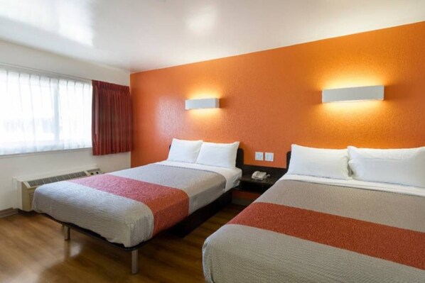 A hotel room with two beds, a window with curtains, a wall-mounted nightstand, and a thermostat.