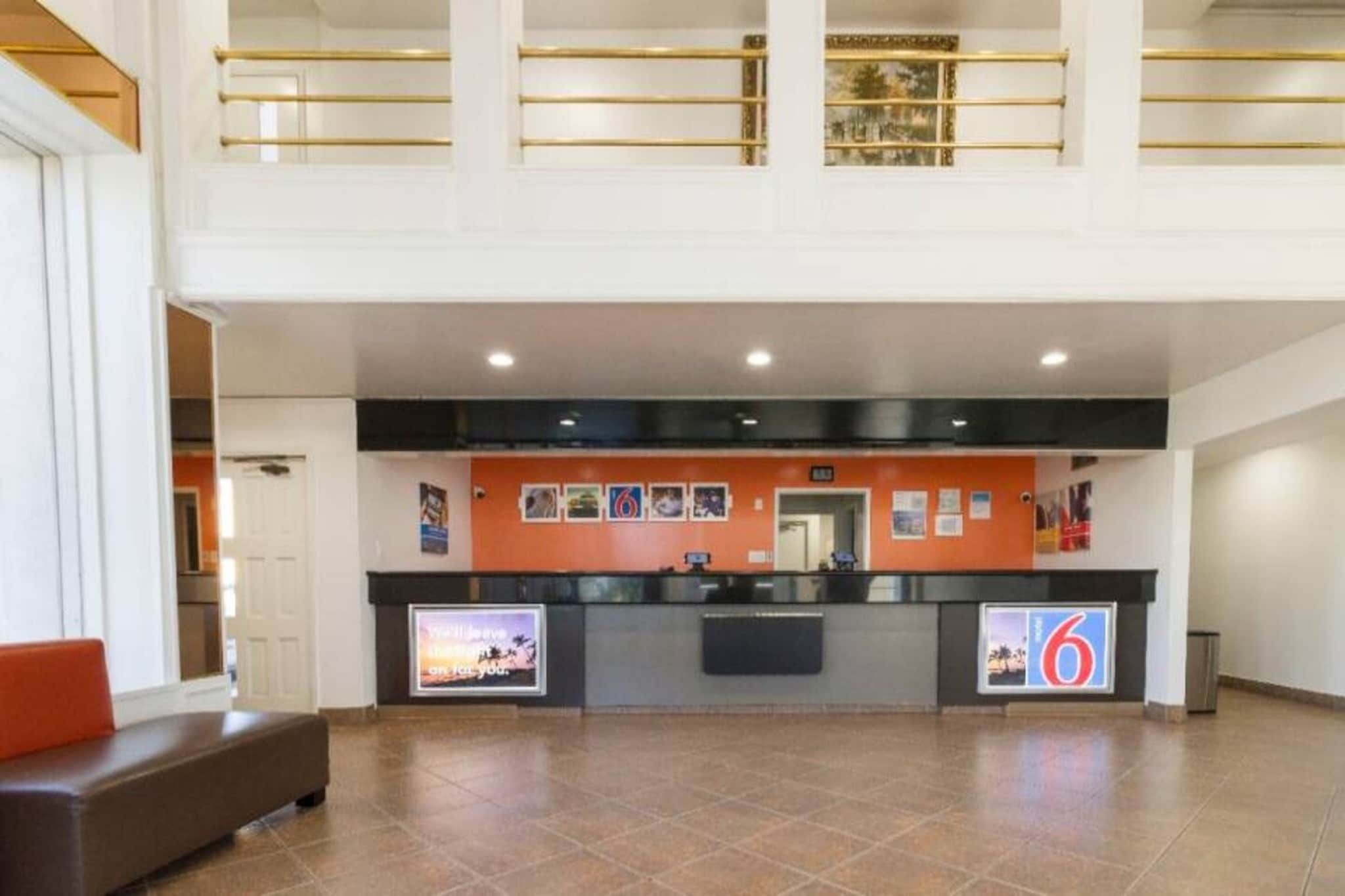 A hotel reception area with a counter, a bench, and a view of the upper floor.
